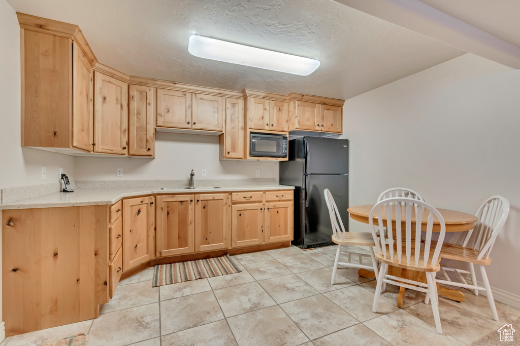 Kitchen with black appliances, light brown cabinetry, light countertops, a sink, and a textured ceiling