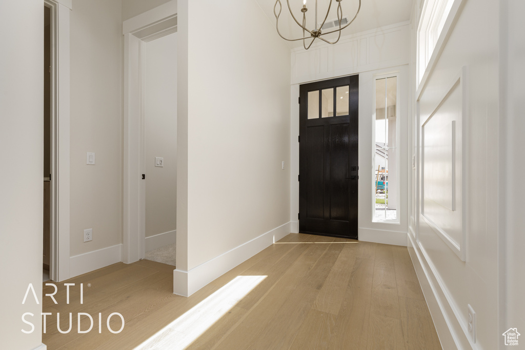 Foyer featuring light wood finished floors, a chandelier, plenty of natural light, and baseboards