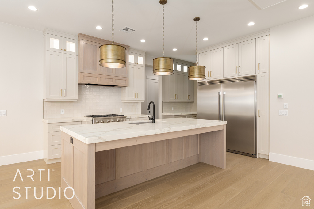 Kitchen with built in refrigerator, a sink, baseboards, tasteful backsplash, and light wood-style flooring