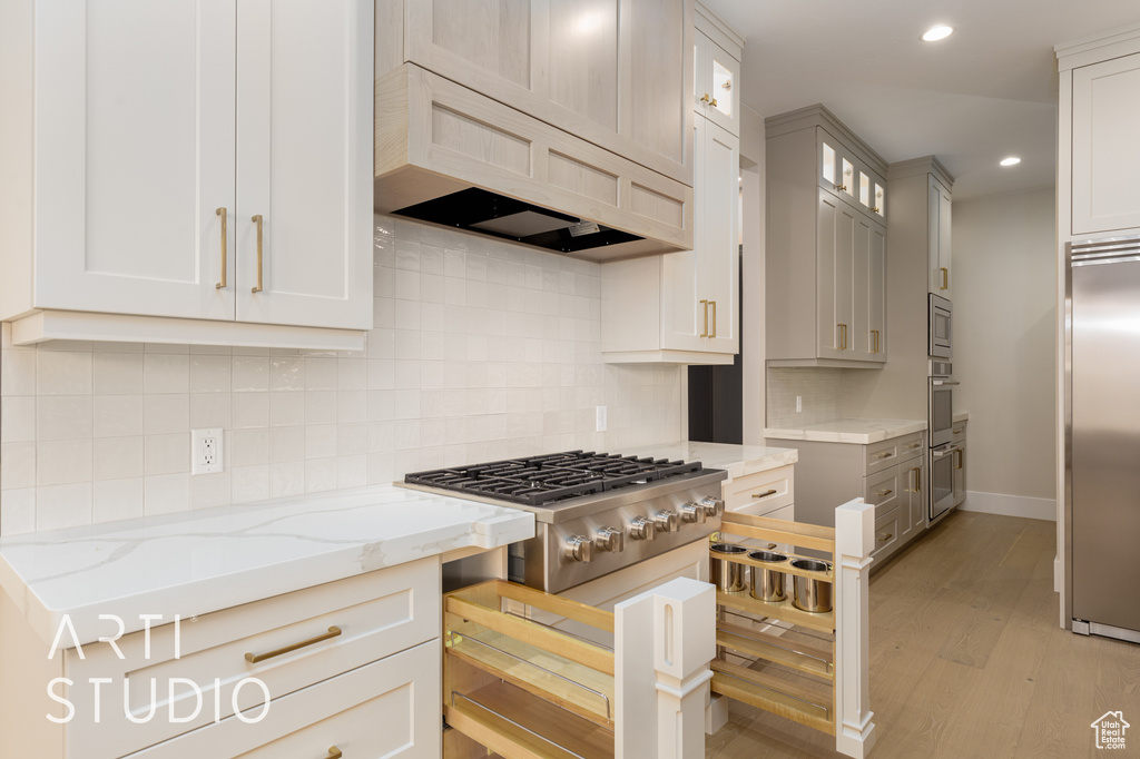 Kitchen with built in appliances, custom range hood, light stone countertops, light wood-style flooring, and glass insert cabinets