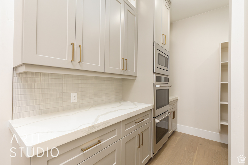 Kitchen with appliances with stainless steel finishes, light wood-type flooring, decorative backsplash, light stone countertops, and baseboards