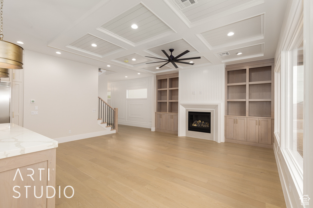 Unfurnished living room featuring coffered ceiling, light wood-style flooring, stairway, built in features, and healthy amount of natural light