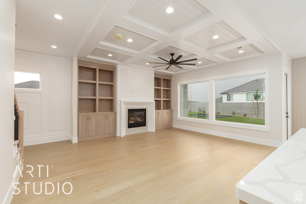 Unfurnished living room featuring light wood-style floors, coffered ceiling, beam ceiling, a glass covered fireplace, and recessed lighting