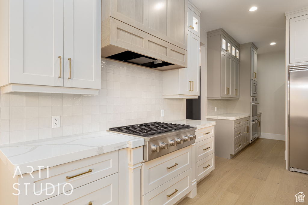 Kitchen with built in appliances, light stone counters, light wood-style flooring, glass insert cabinets, and premium range hood
