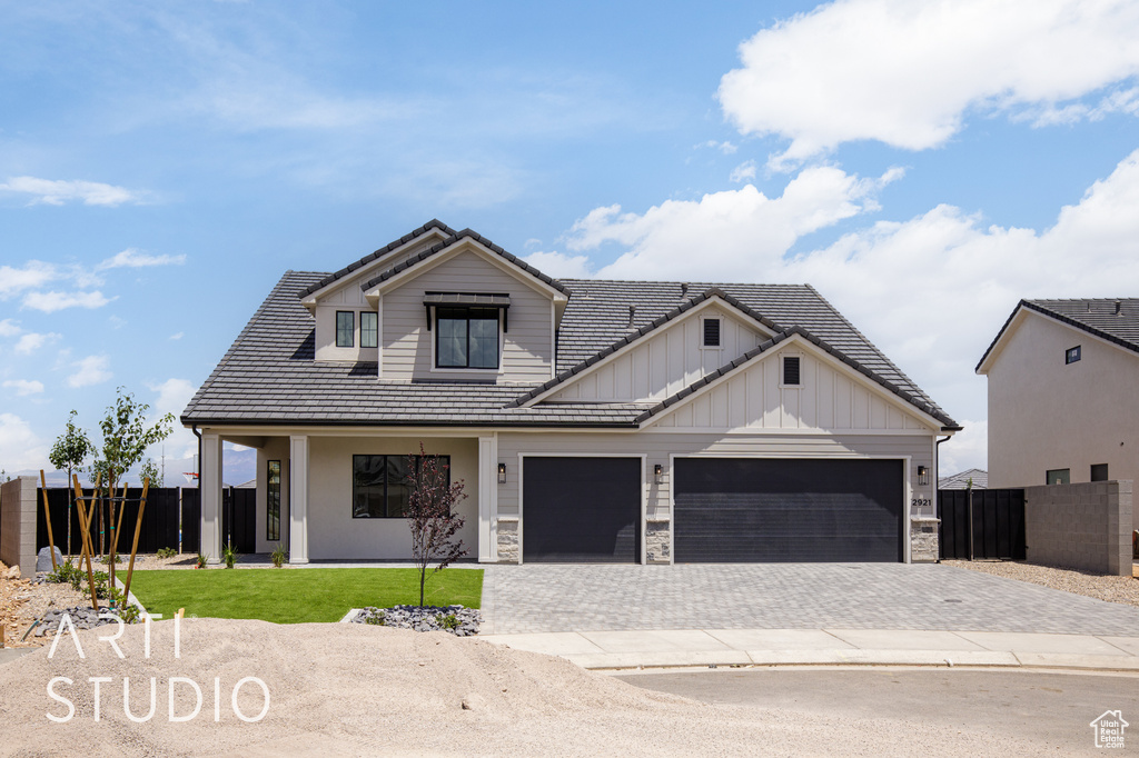 Modern inspired farmhouse with board and batten siding, decorative driveway, an attached garage, a tiled roof, and stone siding