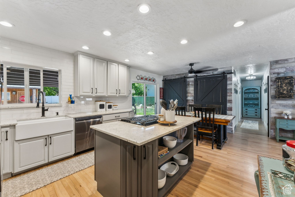 Kitchen with stainless steel dishwasher, a barn door, a sink, open shelves, and light wood-style flooring