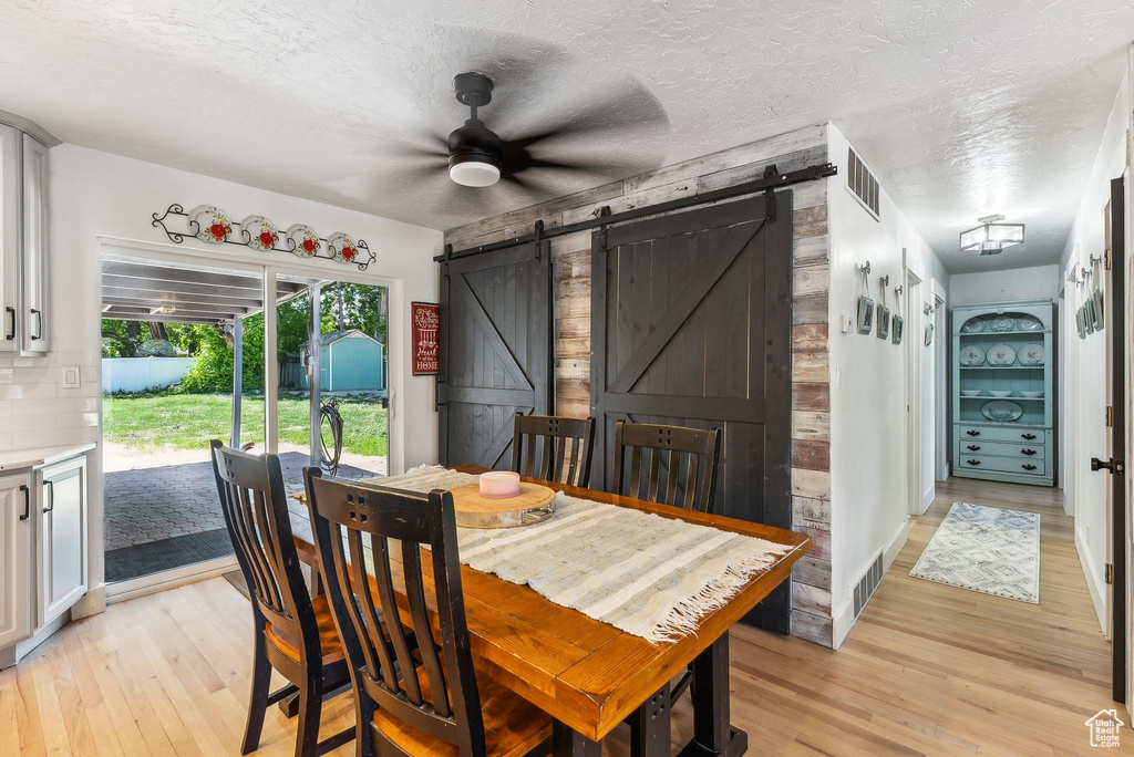 Dining room featuring a barn door, light wood-style flooring, a ceiling fan, and a textured ceiling