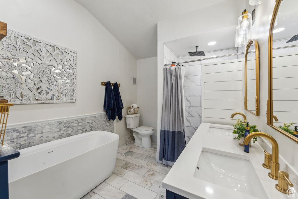 Bathroom featuring double vanity, toilet, a freestanding tub, tiled shower, and vaulted ceiling