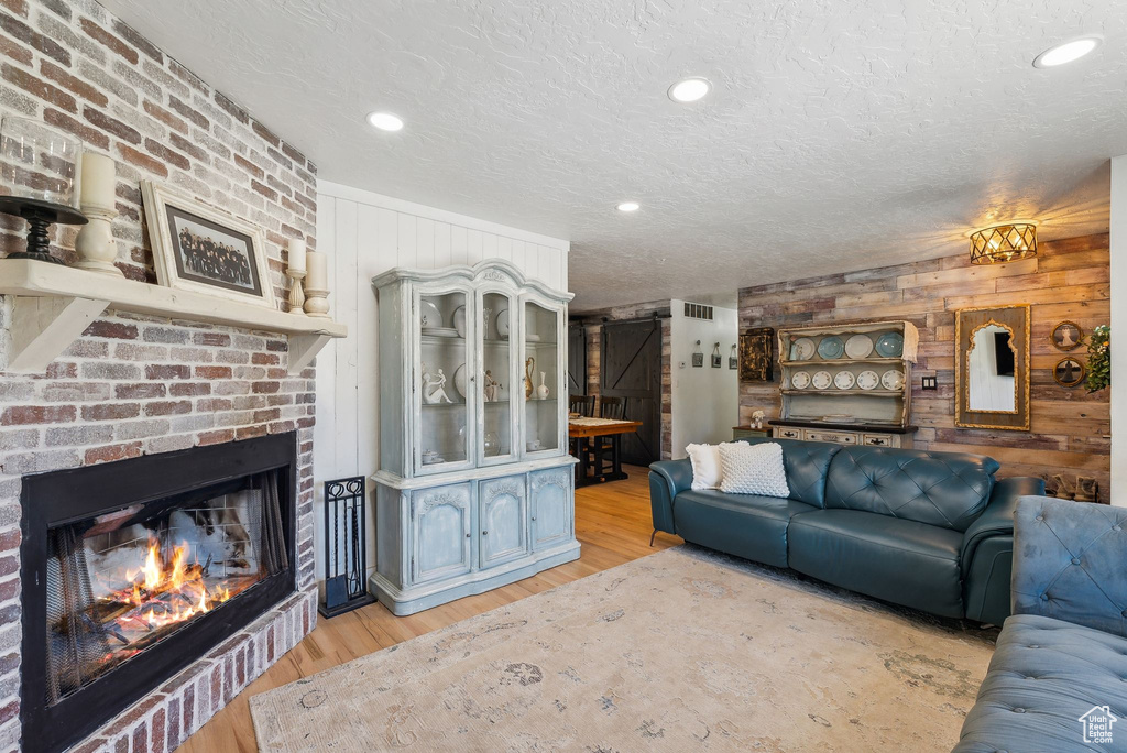 Living area featuring wooden walls, light wood-type flooring, a textured ceiling, a brick fireplace, and recessed lighting