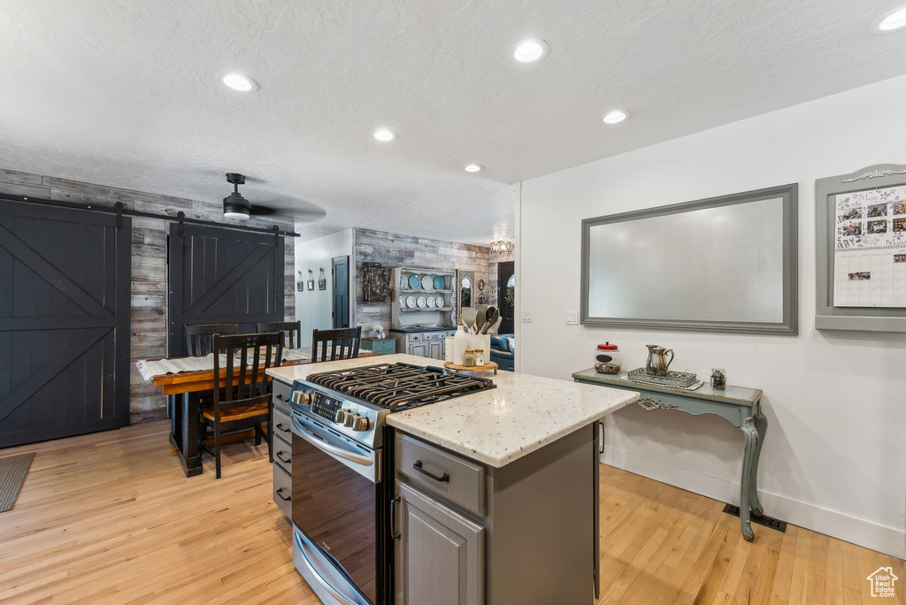 Kitchen with stainless steel gas range oven, a barn door, light wood-type flooring, baseboards, and recessed lighting