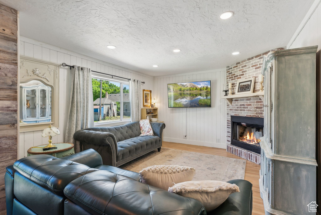 Living room featuring a textured ceiling, light wood-style flooring, a brick fireplace, baseboards, and recessed lighting