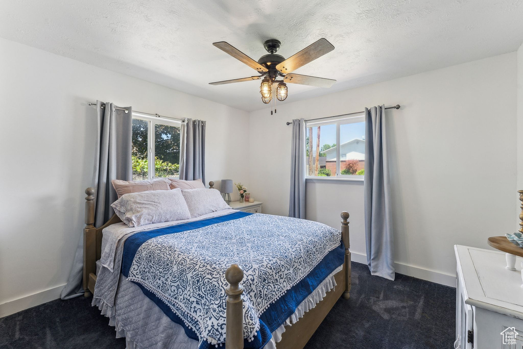 Bedroom with dark carpet, multiple windows, baseboards, and ceiling fan