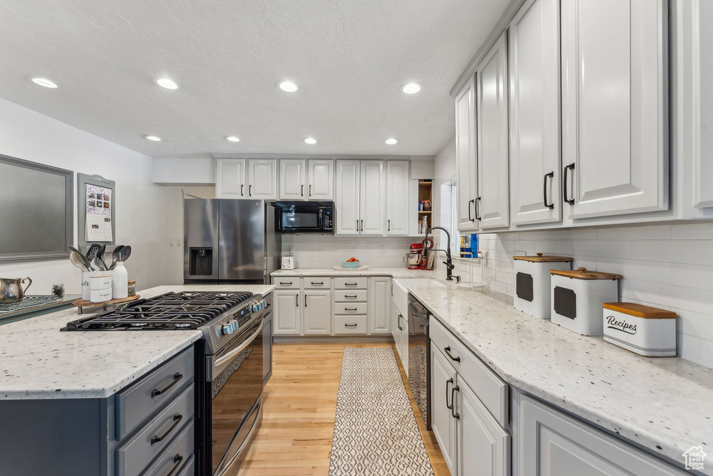 Kitchen with stainless steel appliances, a sink, tasteful backsplash, light wood-style floors, and recessed lighting