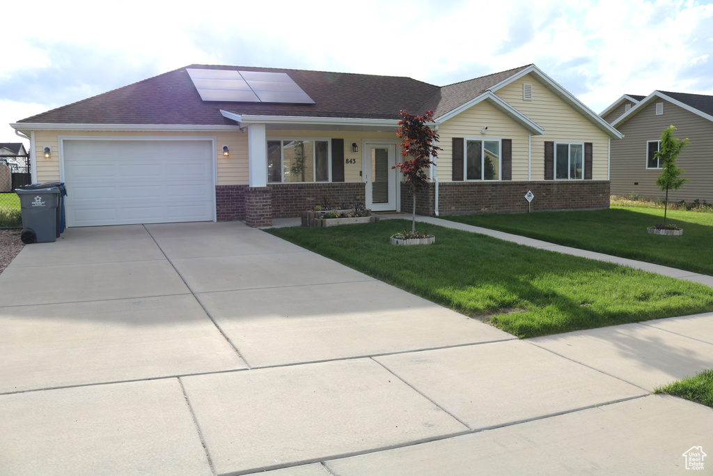 Ranch-style home featuring brick siding, driveway, solar panels, a front yard, and a garage