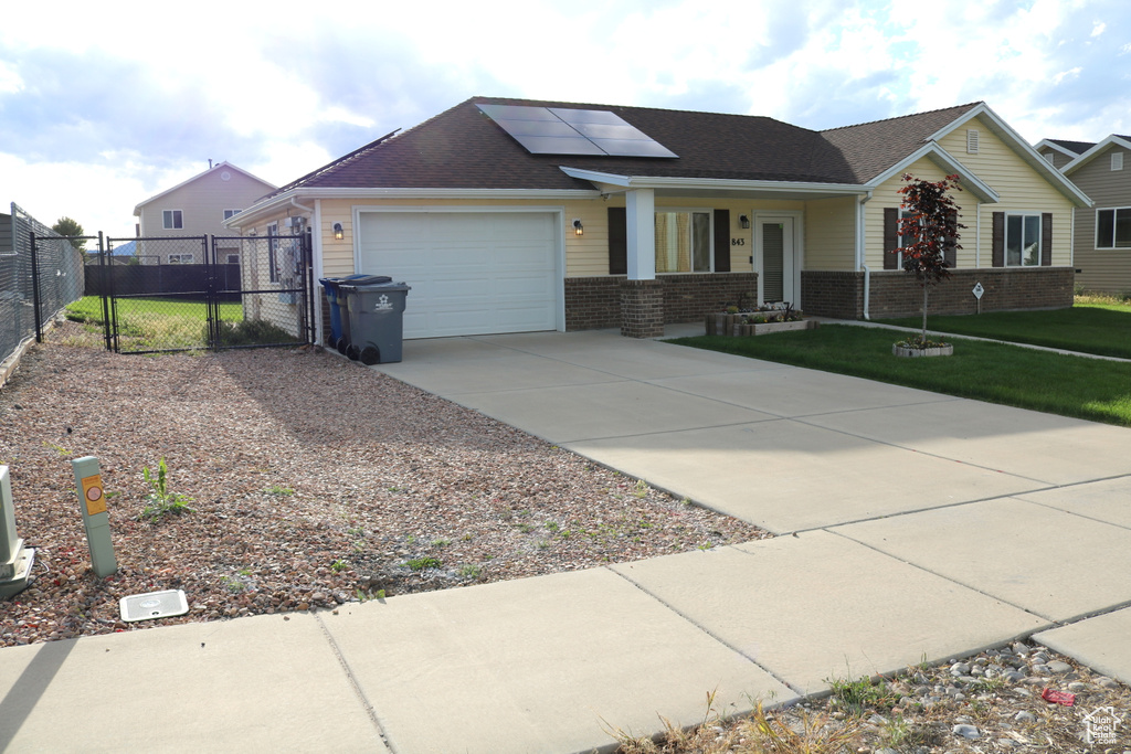 Ranch-style house featuring concrete driveway, a garage, a porch, roof mounted solar panels, and a gate