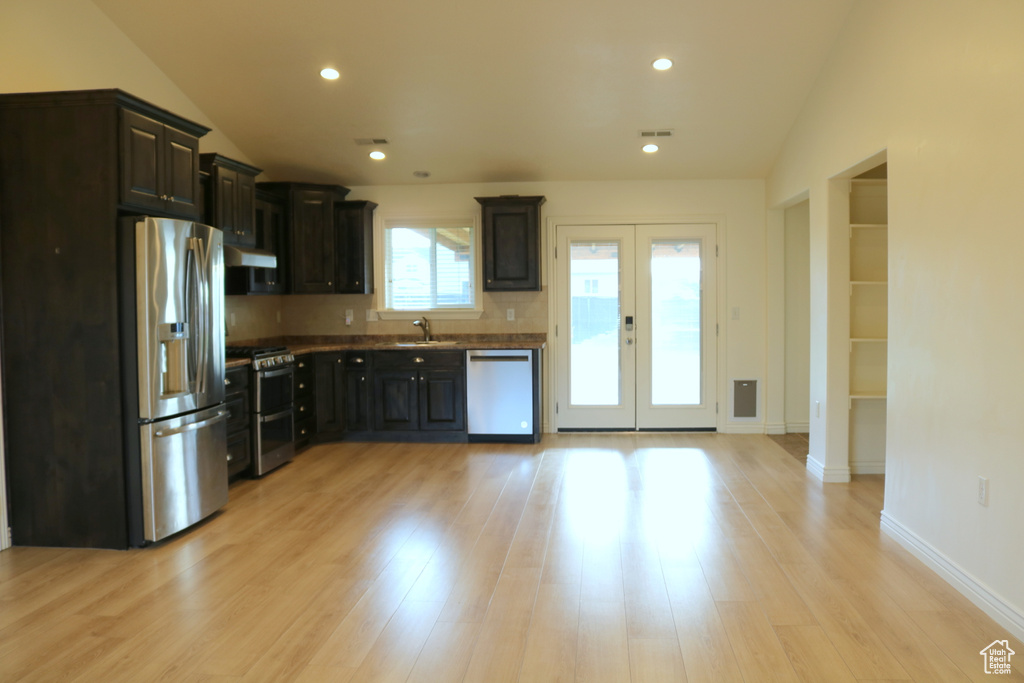 Kitchen with appliances with stainless steel finishes, a sink, range hood, light wood finished floors, and french doors