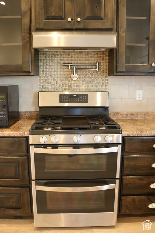 Kitchen featuring double oven range, dark brown cabinets, under cabinet range hood, and glass insert cabinets