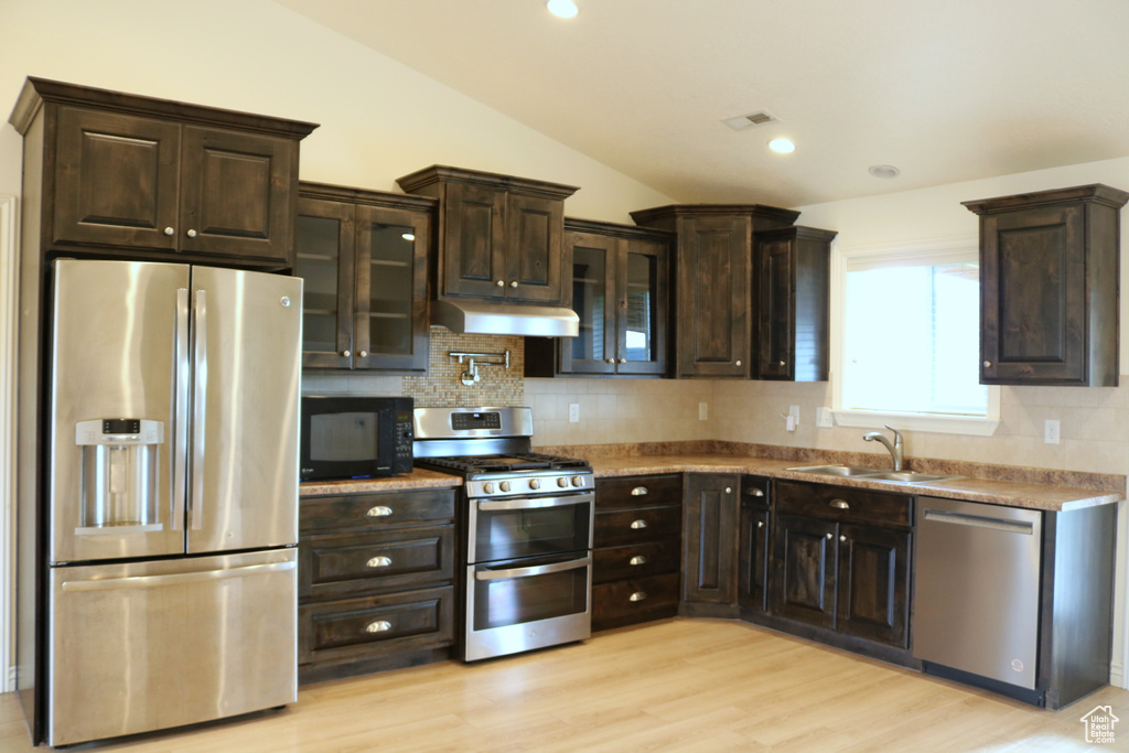 Kitchen with stainless steel appliances, a sink, vaulted ceiling, decorative backsplash, and dark brown cabinets