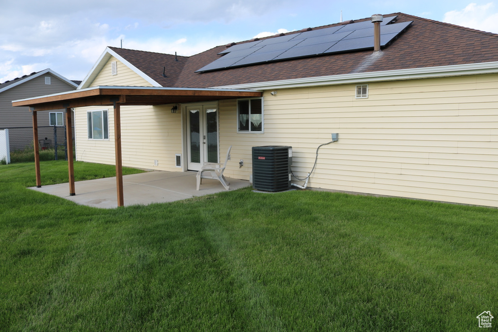 Back of property featuring french doors, central AC unit, a lawn, roof mounted solar panels, and a patio