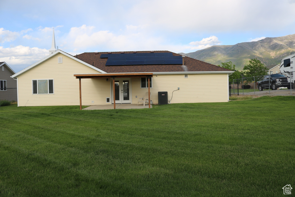 Back of property featuring french doors, solar panels, a patio area, roof with shingles, and a mountain view