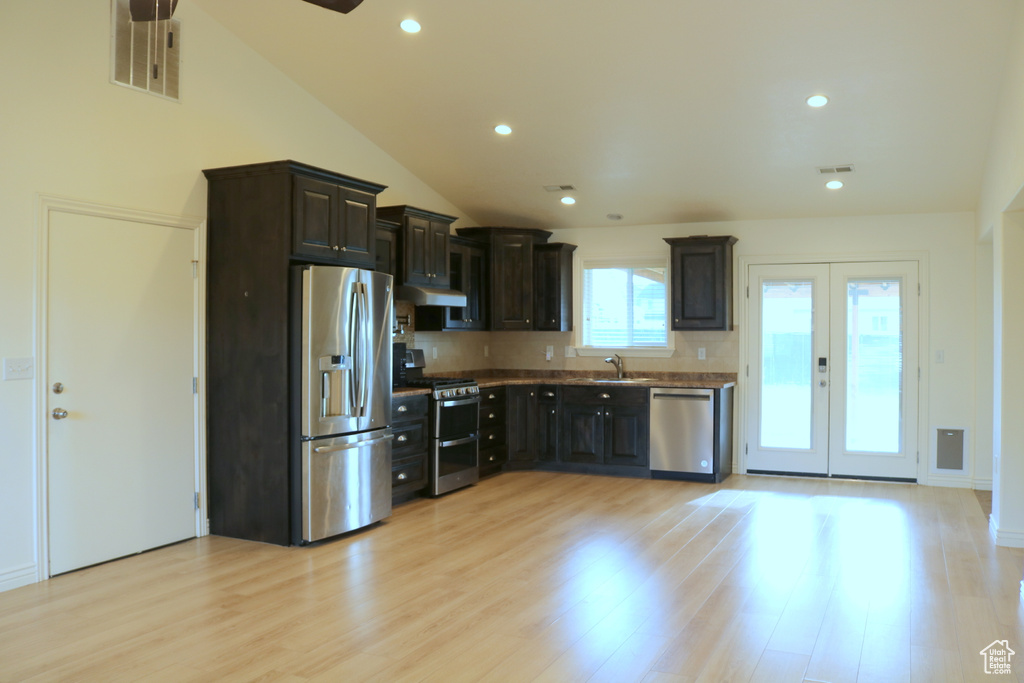 Kitchen featuring stainless steel appliances, a sink, under cabinet range hood, light wood-type flooring, and lofted ceiling