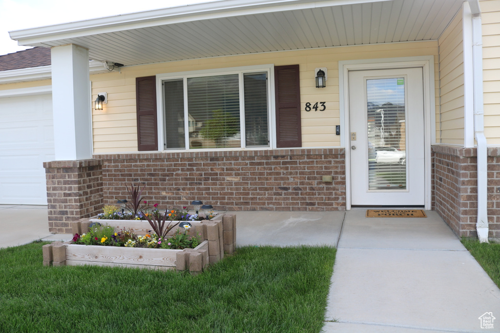 Property entrance with brick siding, an attached garage, and covered porch