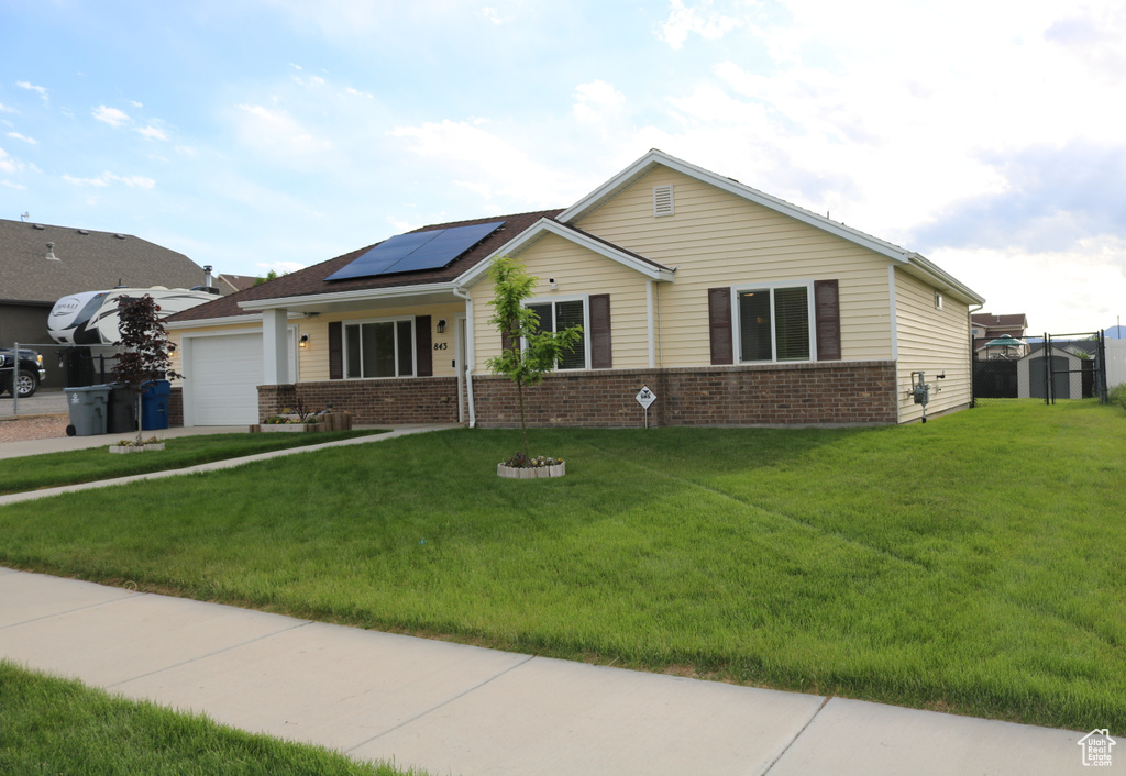 Single story home featuring a garage, brick siding, roof mounted solar panels, and a front yard