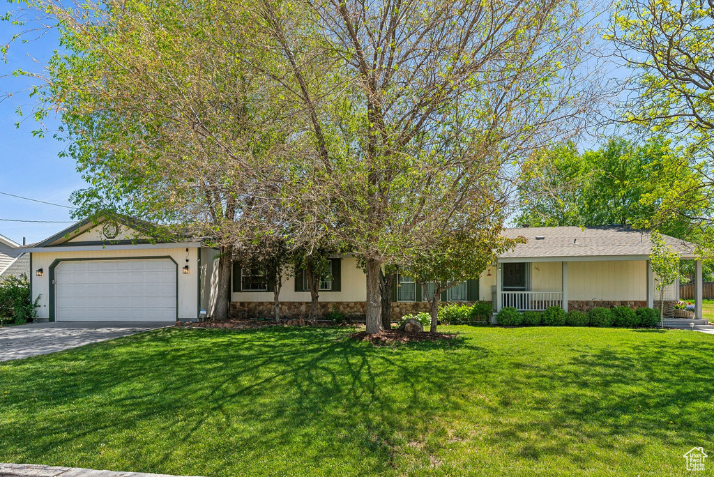 Single story home featuring an attached garage, a front lawn, stone siding, and driveway