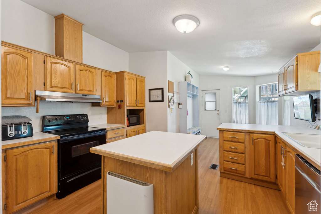 Kitchen with black appliances, light wood-type flooring, under cabinet range hood, light countertops, and a kitchen island