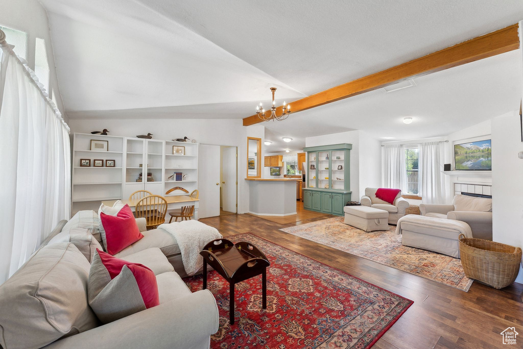 Living room with vaulted ceiling, wood finished floors, a chandelier, and a tile fireplace