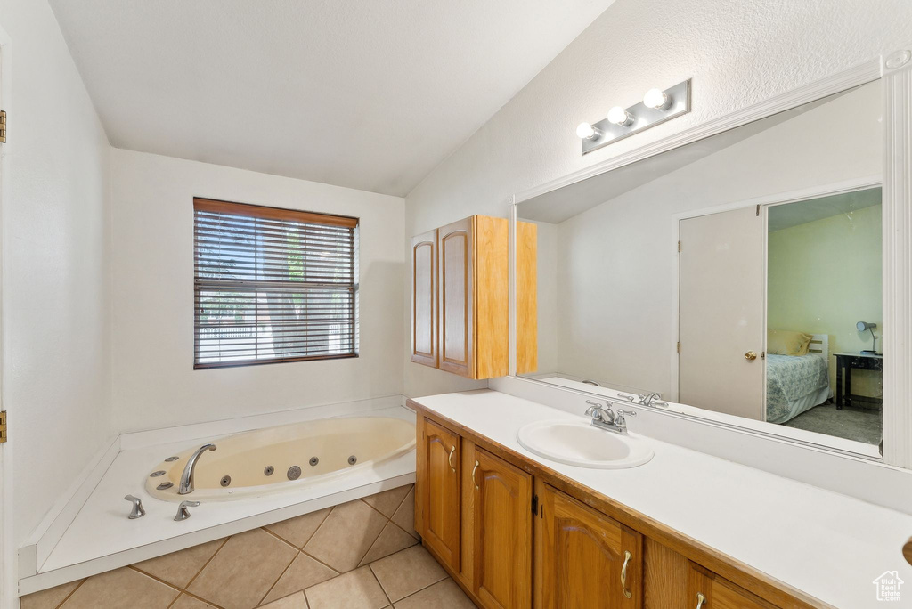 Ensuite bathroom featuring vanity, a tub with jets, lofted ceiling, and tile patterned flooring