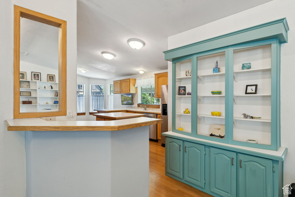 Kitchen with appliances with stainless steel finishes, a peninsula, light wood finished floors, light countertops, and a sink