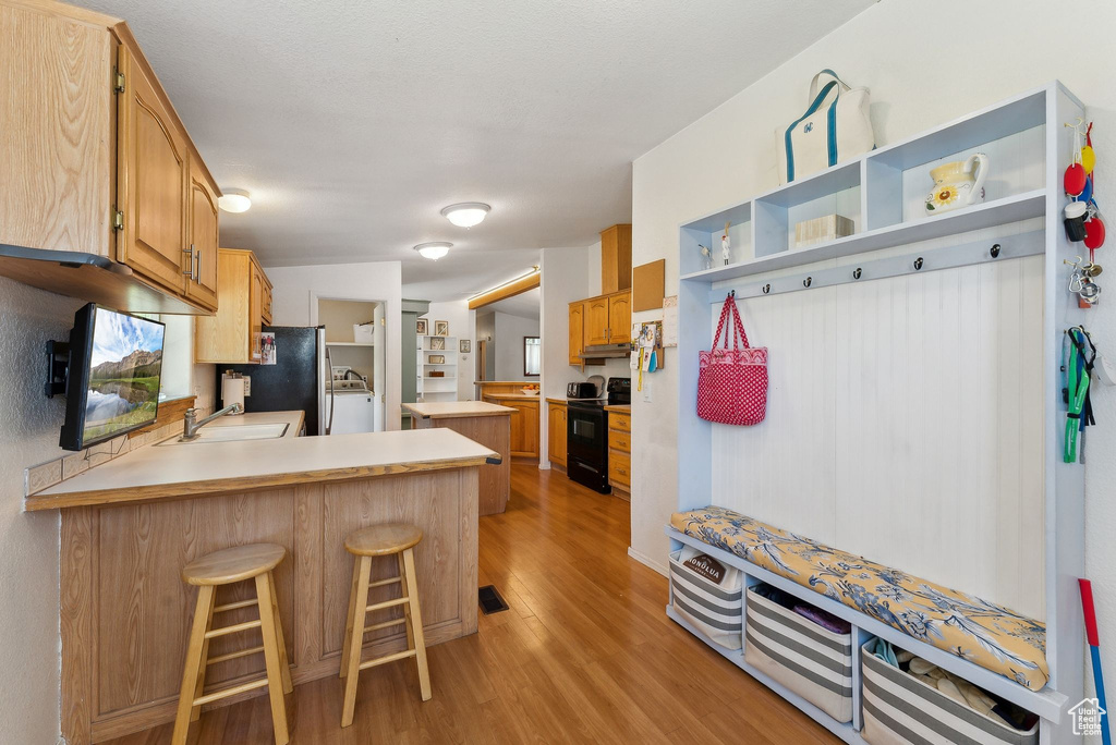 Kitchen with electric range, a sink, washer / dryer, a peninsula, and light wood-style floors