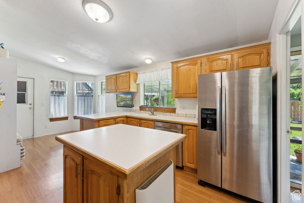 Kitchen featuring appliances with stainless steel finishes, light countertops, light wood-style floors, a peninsula, and a sink
