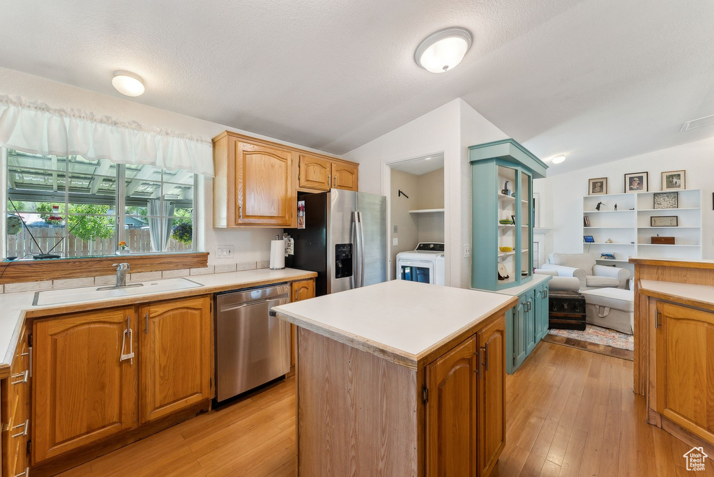 Kitchen with appliances with stainless steel finishes, vaulted ceiling, a sink, and light countertops