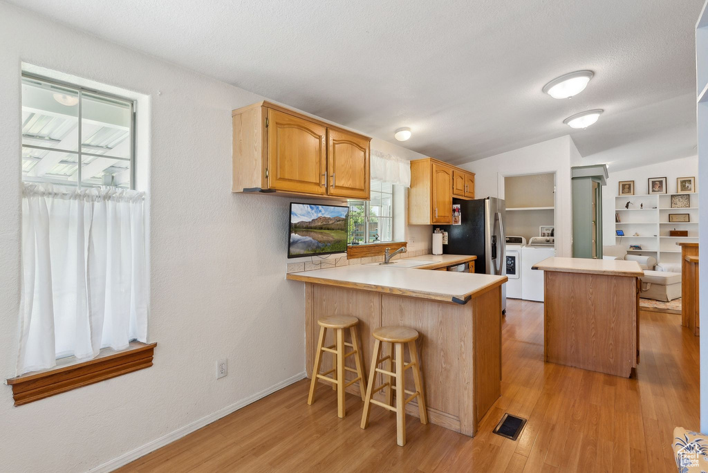 Kitchen featuring a sink, light countertops, stainless steel fridge, light wood-style flooring, and lofted ceiling