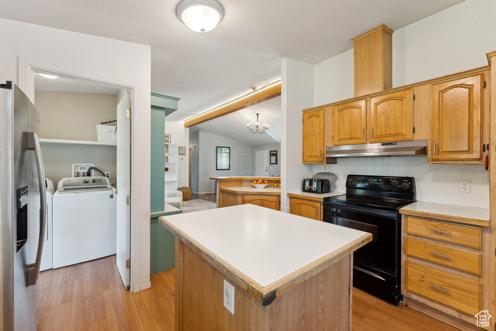 Kitchen with black electric range oven, under cabinet range hood, separate washer and dryer, stainless steel fridge, and light wood finished floors