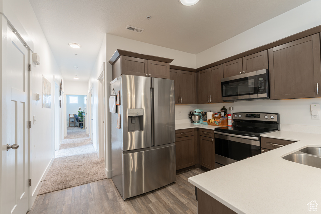 Kitchen featuring appliances with stainless steel finishes, light wood-style floors, light countertops, and dark brown cabinets