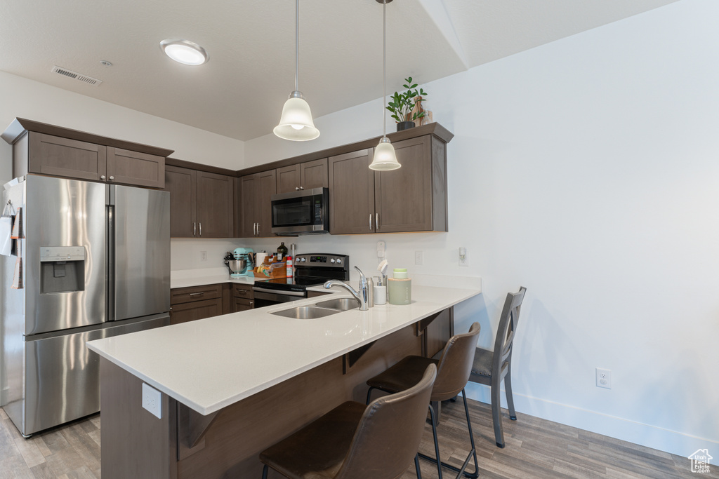 Kitchen with appliances with stainless steel finishes, a sink, light wood-type flooring, a peninsula, and a kitchen bar