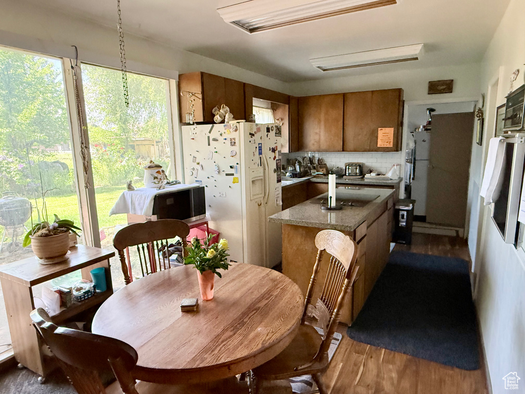 Kitchen with white refrigerator with ice dispenser, brown cabinets, dark wood-style floors, and decorative backsplash