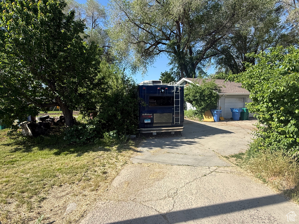 View of property hidden behind natural elements with asphalt driveway
