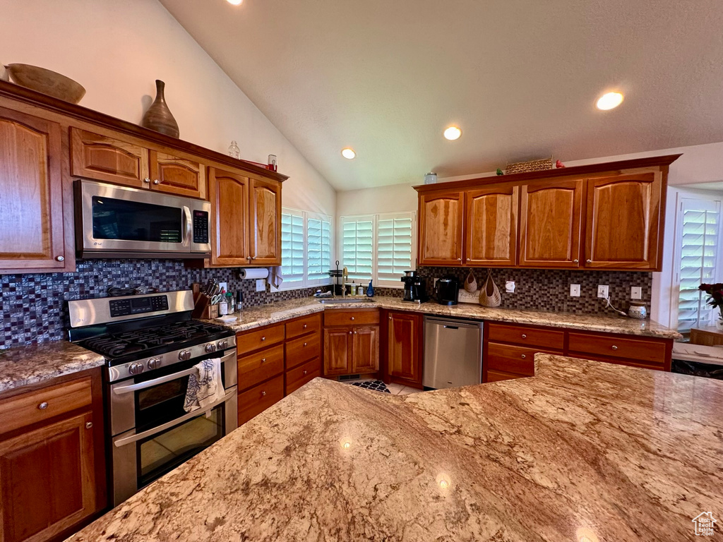 Kitchen with appliances with stainless steel finishes, vaulted ceiling, light stone countertops, tasteful backsplash, and recessed lighting