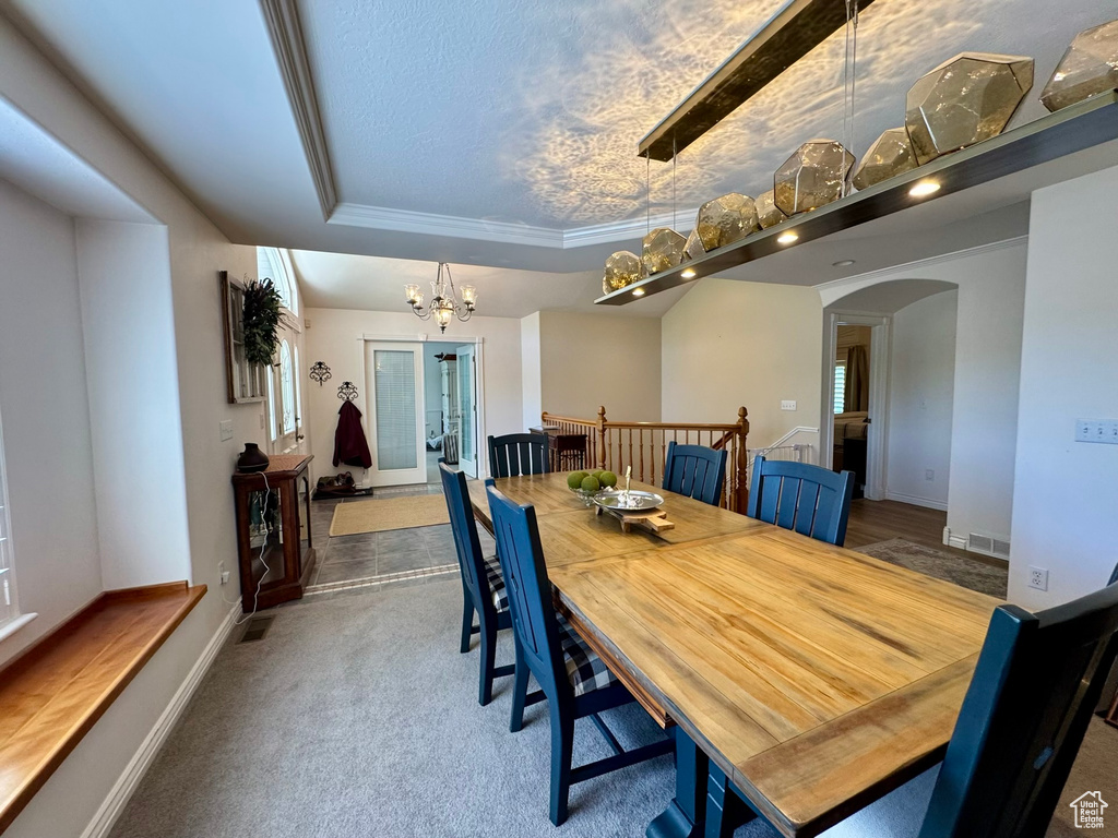 Dining space with arched walkways, a chandelier, carpet flooring, a raised ceiling, and baseboards