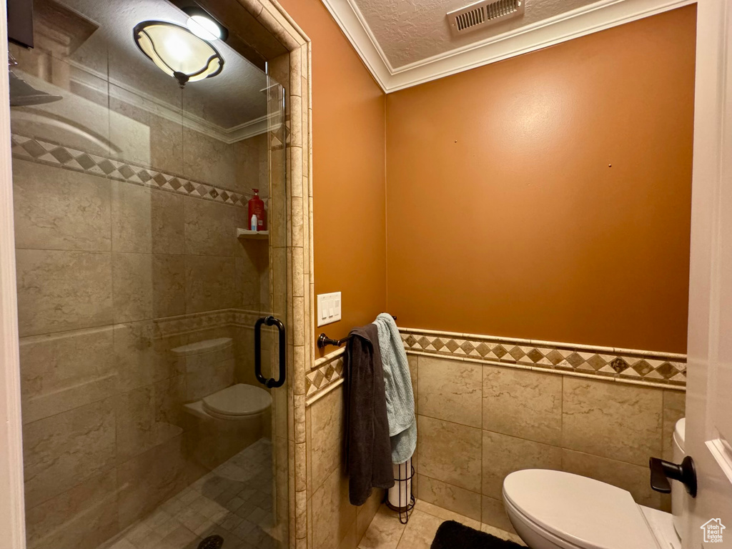 Bathroom featuring toilet, ornamental molding, a shower stall, tile walls, and wainscoting