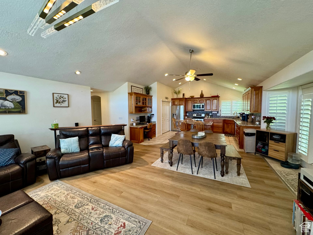 Living room featuring vaulted ceiling, ceiling fan, light wood-type flooring, a textured ceiling, and recessed lighting