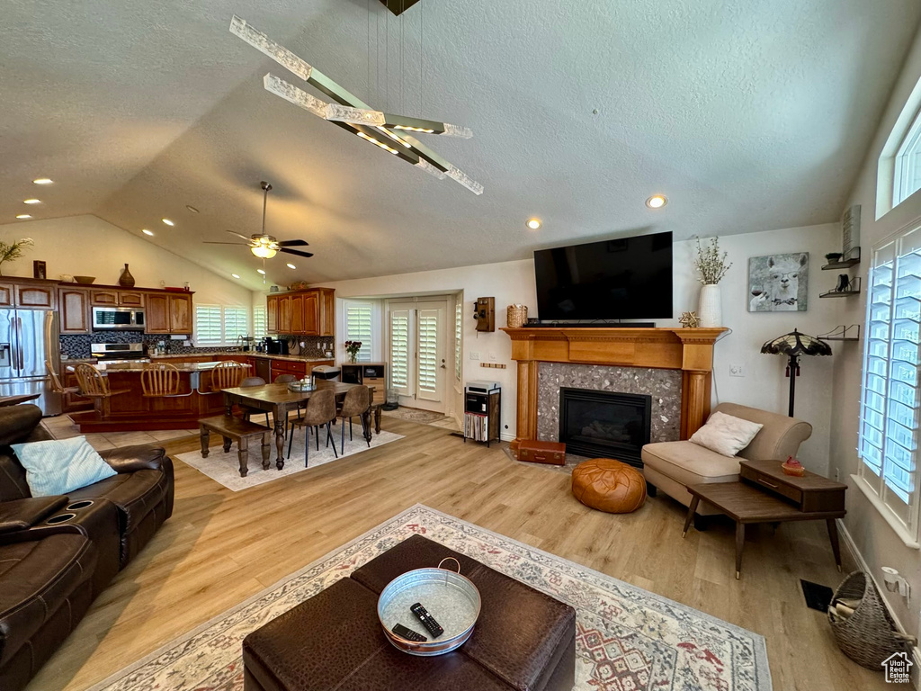 Living area featuring a ceiling fan, lofted ceiling, a textured ceiling, light wood-type flooring, and a tile fireplace