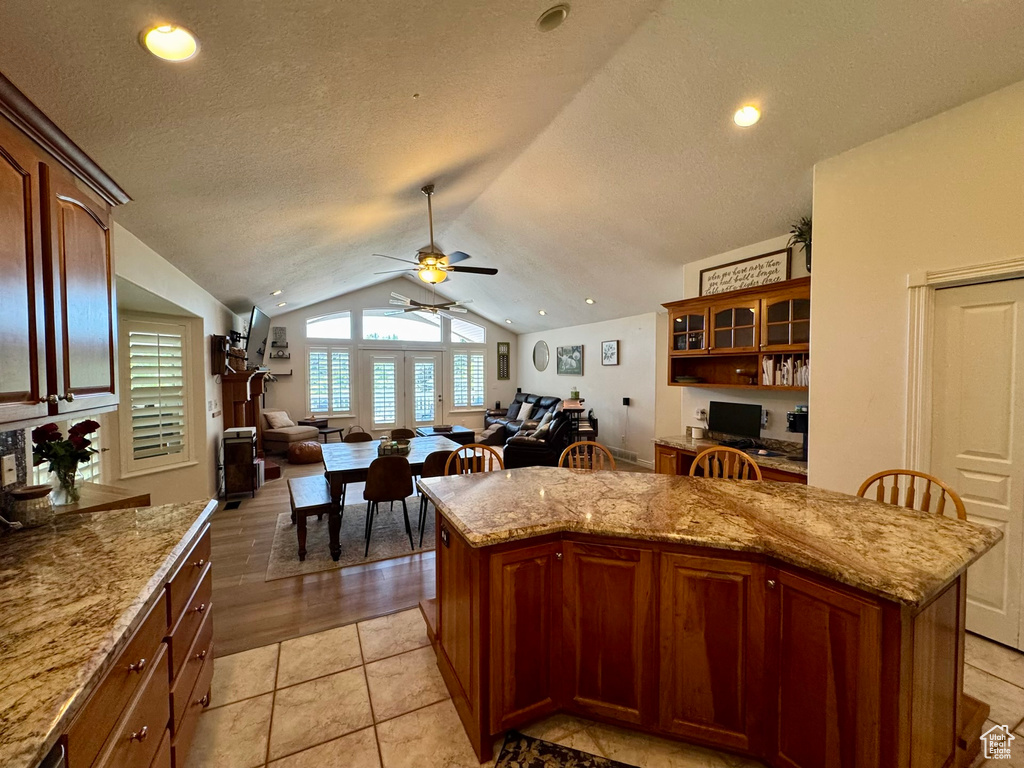 Kitchen featuring vaulted ceiling, a ceiling fan, open floor plan, a kitchen island, and light stone counters