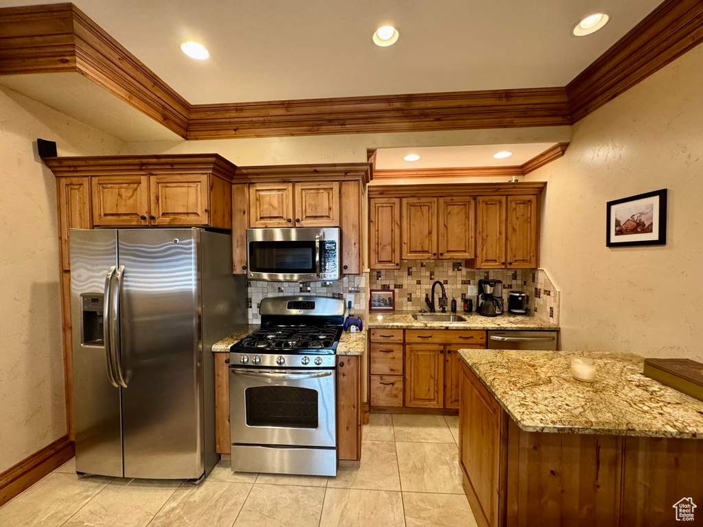 Kitchen with stainless steel appliances, a sink, crown molding, tasteful backsplash, and brown cabinets