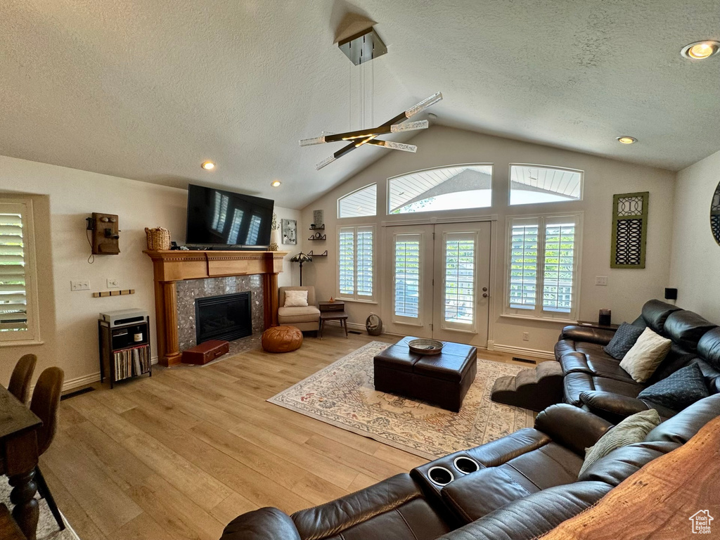 Living area featuring a textured ceiling, light wood-type flooring, lofted ceiling, a fireplace, and baseboards