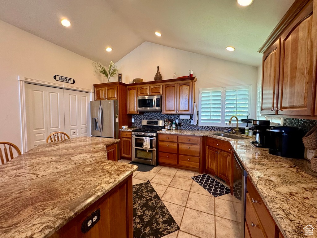 Kitchen featuring stainless steel appliances, a sink, tasteful backsplash, light stone counters, and vaulted ceiling